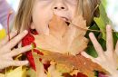 girl looking at camera and playing with a bunch of autumn leaves