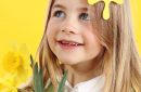 Portrait little blonde girl on yellow background with spring daffodil flowers