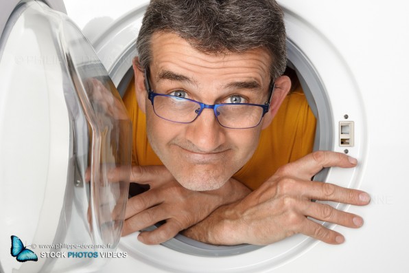 photo fun et comique d'un homme de 45, 50 ans à l'intérieur d'une machine à laver le linge, vue de l'exterieur coté hublot