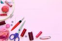 Sewing accessories on a pink background with needles, spool of thread, scissors and a tape measure