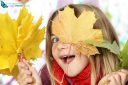 girl hiding behind autumn leaves looking at the camera