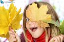 girl hiding behind autumn leaves looking at the camera