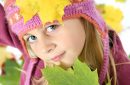 Portrait of little girl in autumn with multicolored leaves and in woolen cap.