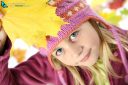 Portrait of little girl in autumn with yellow leaves and in woolen cap.