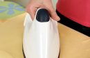 A woman's hand picks up a steam iron from an ironing board