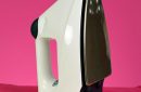 A steam iron on an ironing board and pink background