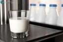 Close-up glass of milk on fridge door with four plastic milk bottles