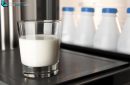 Close-up glass of milk on fridge door with four plastic milk bottles
