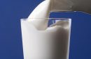 carafe of milk pouring into a glass to the brim and isolated on blue background