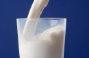 Milk from jug poured into a glass. Milk overflows on the table