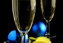 Close up of two champagne glasses, blue Christmas balls and confetti on black background