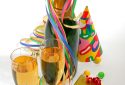 bottle and glass of champagne, paper ribbon, confetti, party hats and gifts on white background.