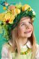 Little smiling blonde girl wearing a costume of yellow Easter eggs, spring flowers and bird feathers on green background.