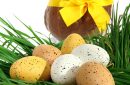 Basket of Easter eggs placed on fresh grass with a big chocolate hen with a yellow node on a white background
