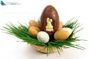 Big chocolate Easter eggs with small ones in a basket with green grass on white