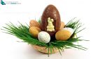 Big chocolate Easter eggs with small ones in a basket with green grass on white
