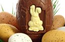 basket of Easter eggs on green grass with a large chocolate egg and a white rabbit