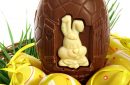 Basket of yellow Easter eggs laid on fresh grass with a large chocolate egg on white background