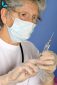 Senior female doctor with mask preparing syringe for injection of COVID-19 vaccine