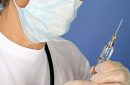 Senior female doctor with mask preparing syringe for injection of COVID-19 vaccine