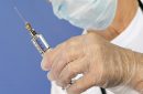 old nurse with protective mask and gloves prepares injection of vaccine or medicine for disease prevention with glass syringe and large needle