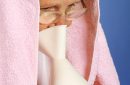 Elderly woman with towel over head inhales essential oil vapor to treat colds and sore throat